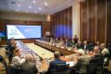 Reunião formal do Conselho Gestor Estadual em auditório amplo. Mais de vinte pessoas, em trajes sociais e casuais finos, estão sentadas ao redor de uma grande mesa de madeira em formato de U. Ao fundo, um grande painel de LED exibe o slide da "4ª Reunião do Conselho Gestor Estadual", com o logotipo "Paraná Produtivo".
