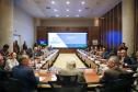 Reunião presencial do Conselho Gestor Estadual em auditório com grande mesa em formato de U. Mais de 20 participantes, vestindo trajes sociais e casuais finos, estão sentados ao redor da mesa. Ao fundo, um painel de LED exibe o slide da "4ª Reunião do Conselho Gestor Estadual", com o logotipo "Paraná Produtivo".