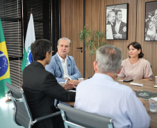 Quatro pessoas conversando à mesa; ao fundo, bandeiras e fotos em preto e branco na parede de madeira.