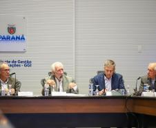 Fotografia mostra quatro homens sentados à mesa de reunião, da esquerda para a direita: Domingos Trevisan Filho (diretor-geral da SEPL), de óculos e terno marrom; Darci Piana (Vice-Governador), de cabelos brancos e terno bege, falando ao microfone; Luizão Goulart (secretário da Administração e da Previdência), de paletó azul e olhando para baixo; e um quarto participante de terno cinza. Ao fundo, na parede branca, destaca-se o brasão do Governo do Paraná e a inscrição "Gabinete de Gestão e Informações - GGI