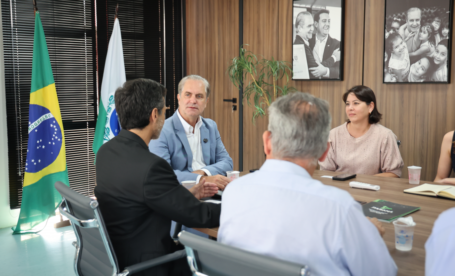 Quatro pessoas conversando à mesa; ao fundo, bandeiras e fotos em preto e branco na parede de madeira.