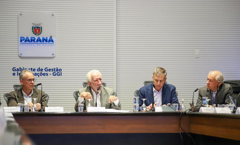 Fotografia mostra quatro homens sentados à mesa de reunião, da esquerda para a direita: Domingos Trevisan Filho (diretor-geral da SEPL), de óculos e terno marrom; Darci Piana (Vice-Governador), de cabelos brancos e terno bege, falando ao microfone; Luizão Goulart (secretário da Administração e da Previdência), de paletó azul e olhando para baixo; e um quarto participante de terno cinza. Ao fundo, na parede branca, destaca-se o brasão do Governo do Paraná e a inscrição "Gabinete de Gestão e Informações - GGI
